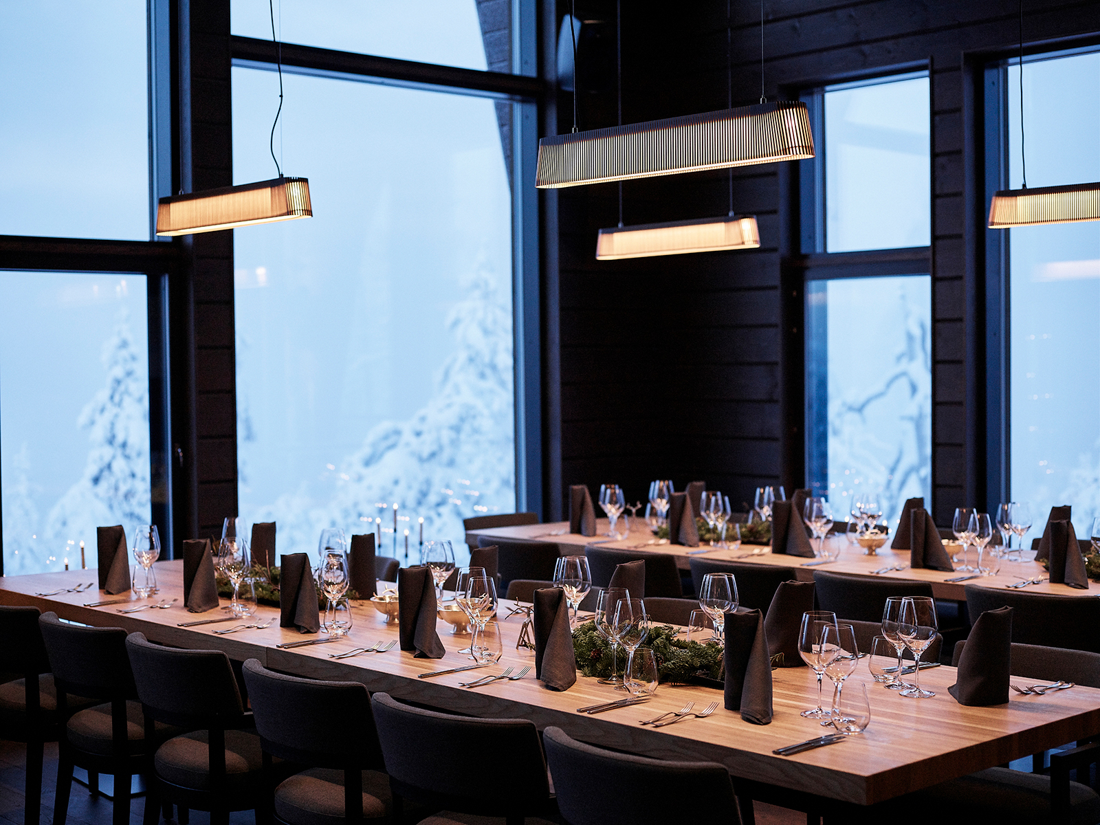 Ein Speisesaal mit Owalo Pendelleuchten. Die Tische sind gedeckt, im Hintergrund zeigen große Fenster eine Winterlandschaft.