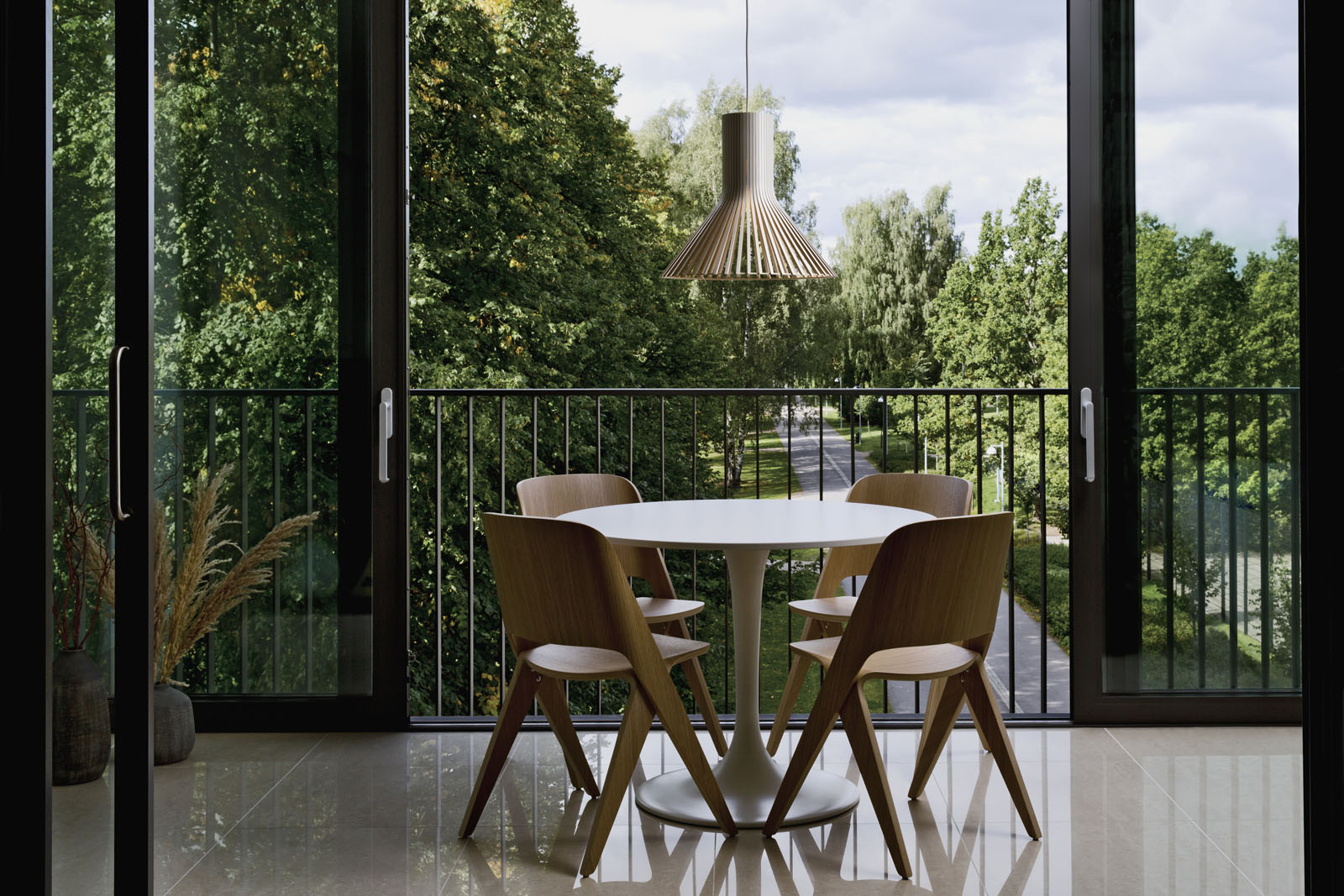 Ein runder Tisch mit vier Stühlen auf einem Balkon. Eine Puncto Pendelleuchte hängt darüber. Im Hindergrund sind Bäume.