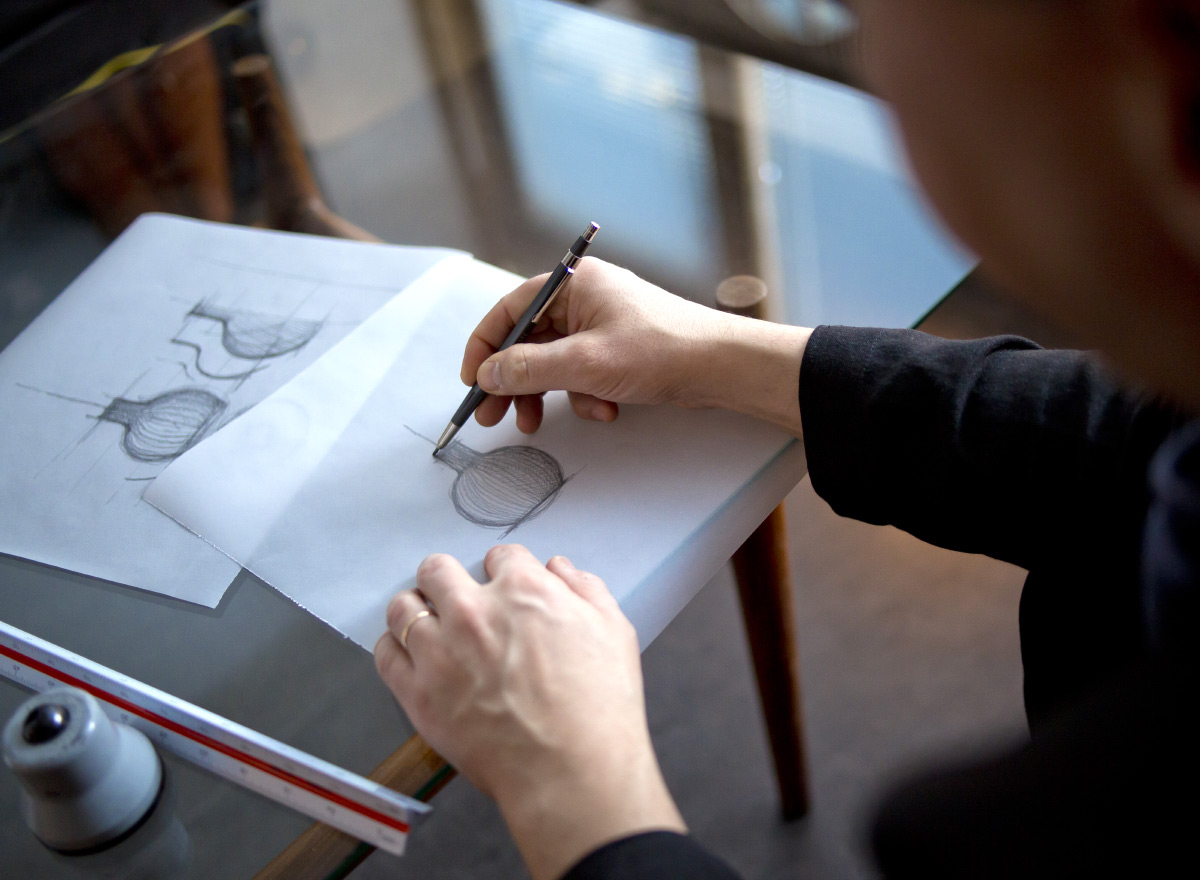 Some sketches of the Octo Small pendant lamp and a ruler on a desk. The designer is sketching.