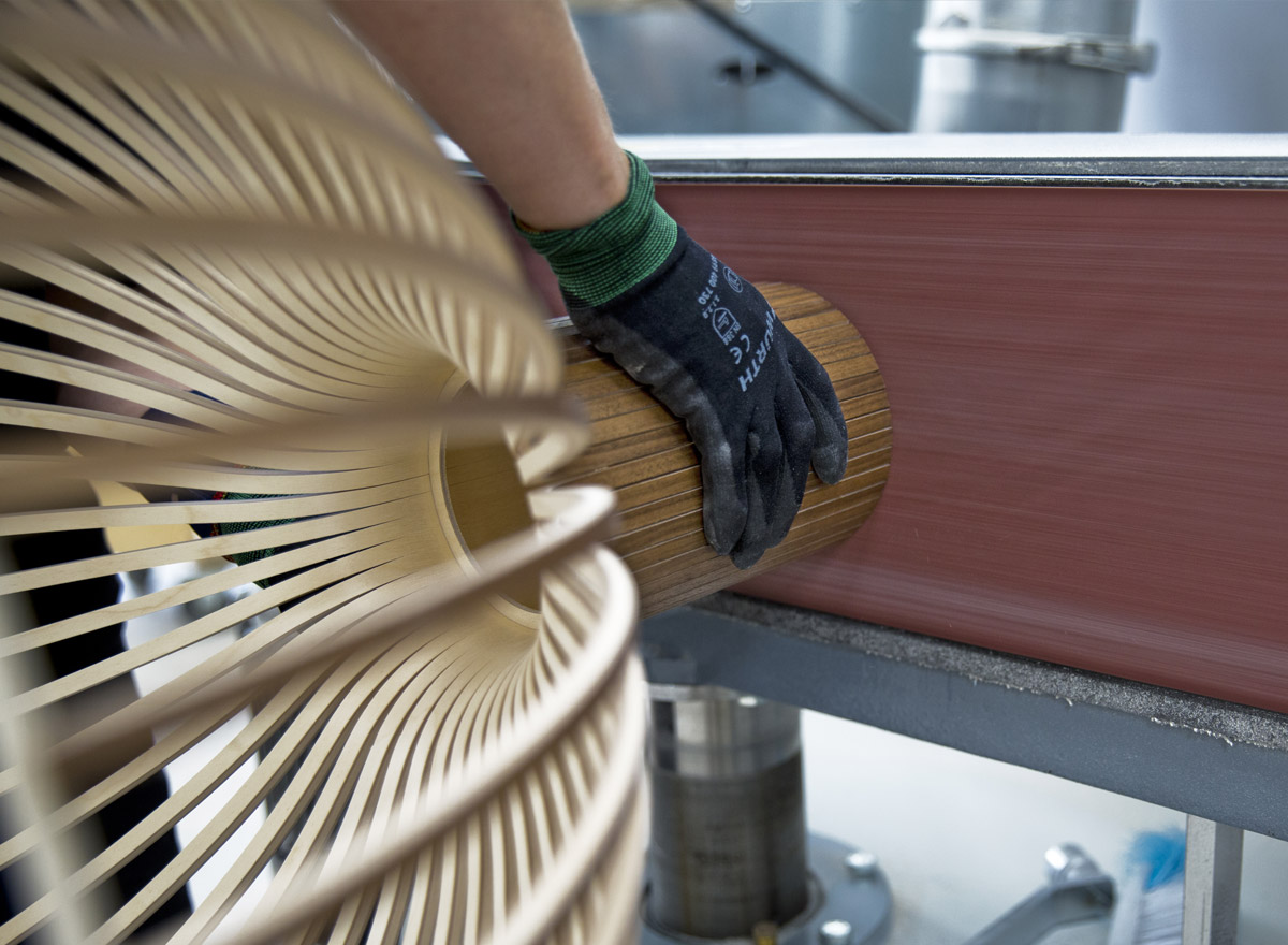 A hand sanding the top of a wooden lampshade.