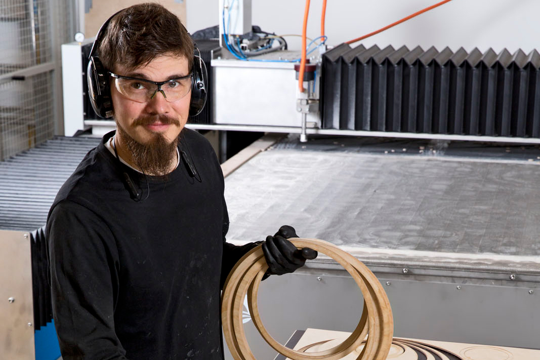 A man wearing safety glasses, gloves and hearing protection, is holding wooden rings.