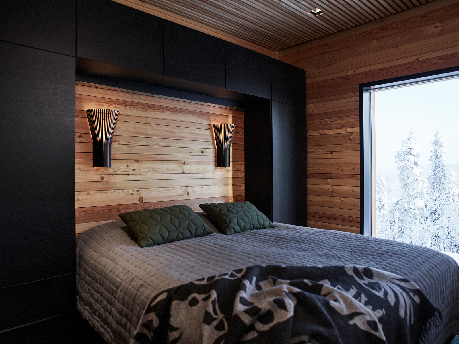 Wall lamps above a large bed and a snowy view from the window.