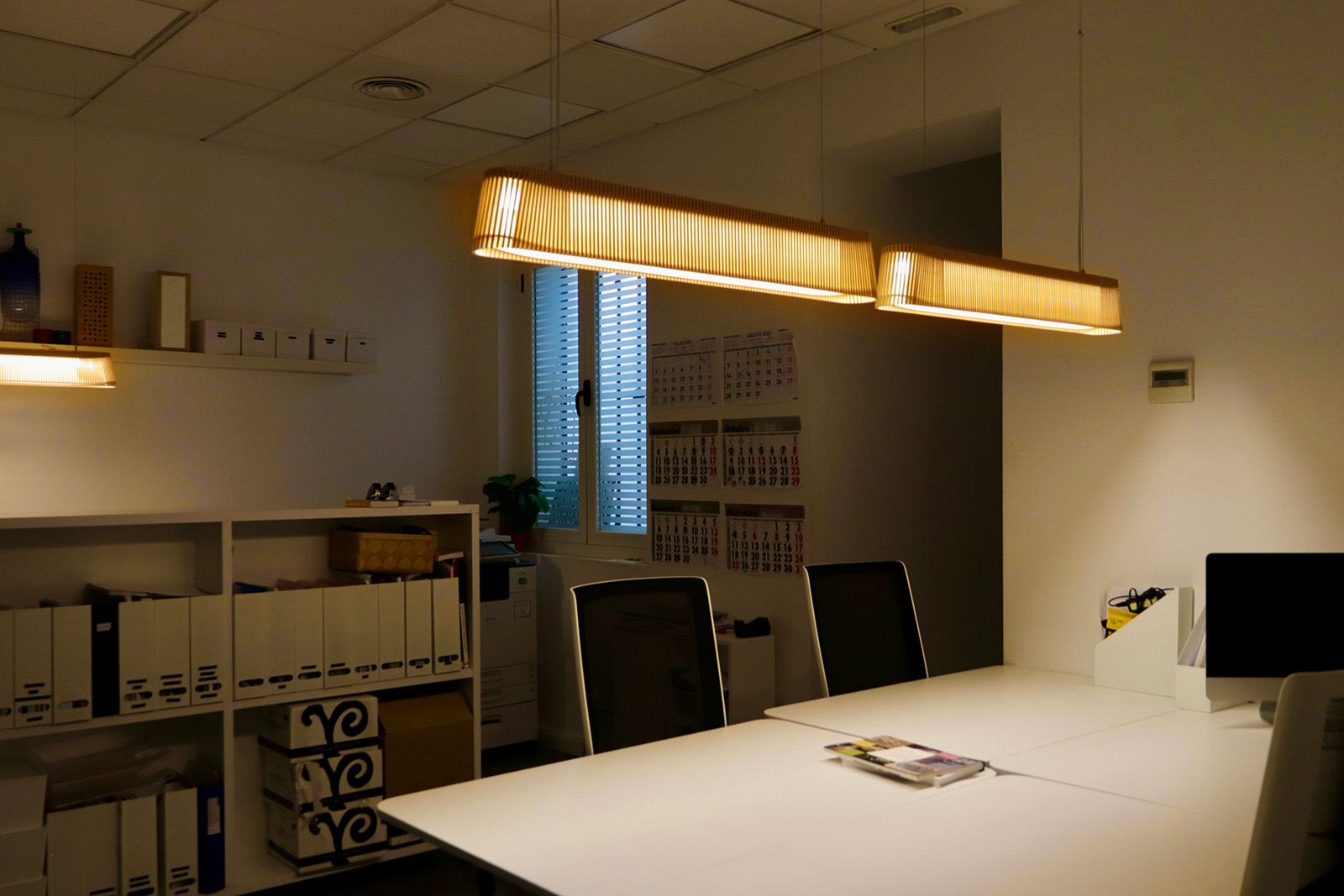 An office lit with three elongated pendant lamps.