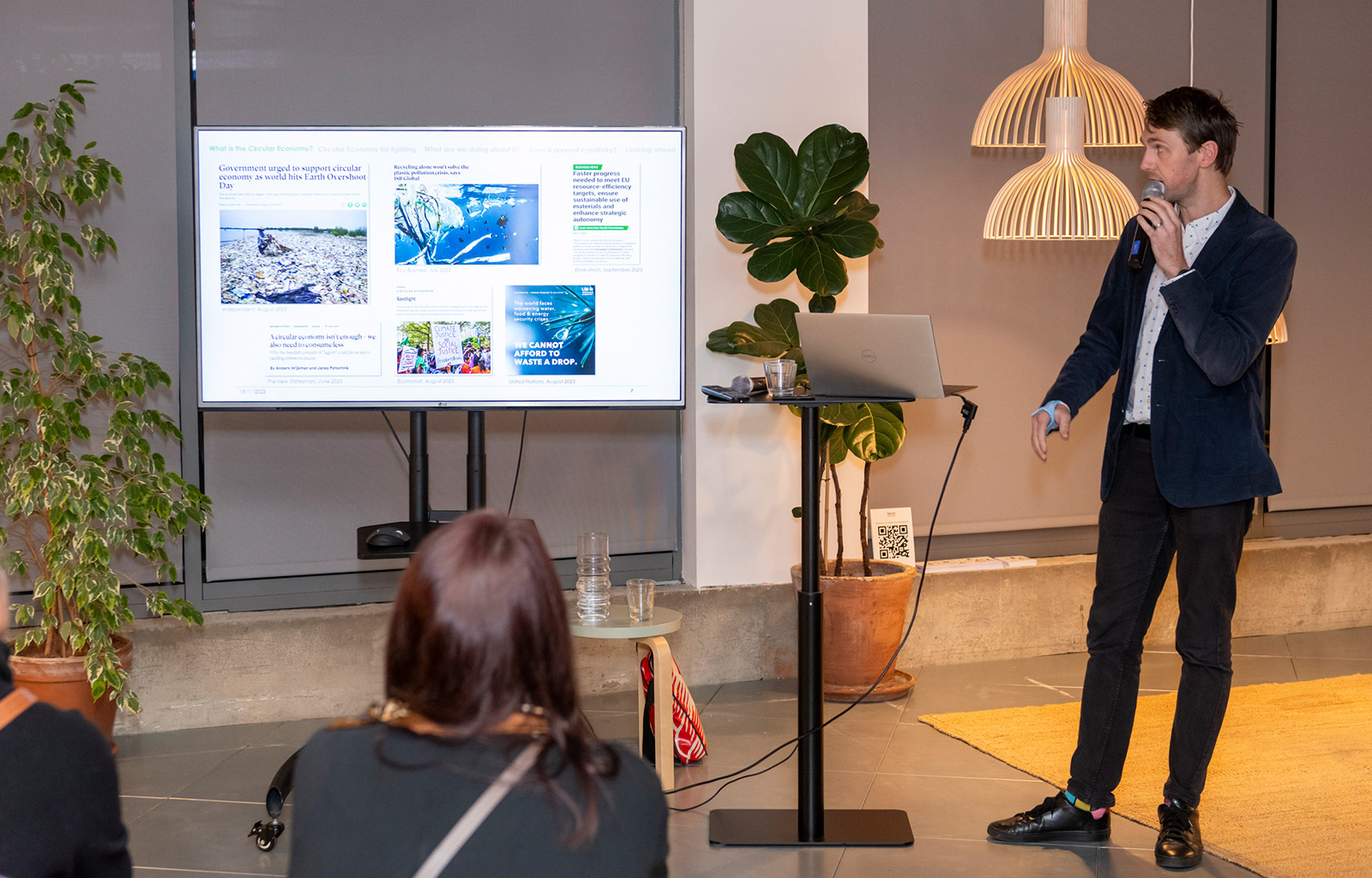 A man in front of the audience talking to a microphone while looking at a presentation on a screen. 