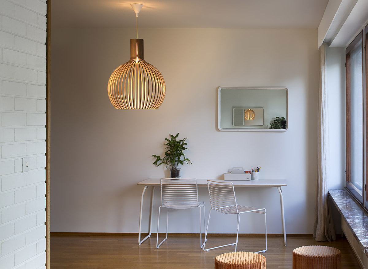 Un ensemble de chaises disposées devant un bureau. Sur le mur, il y a un miroir. La suspension Octo en noyer se trouve au milieu de la pièce.