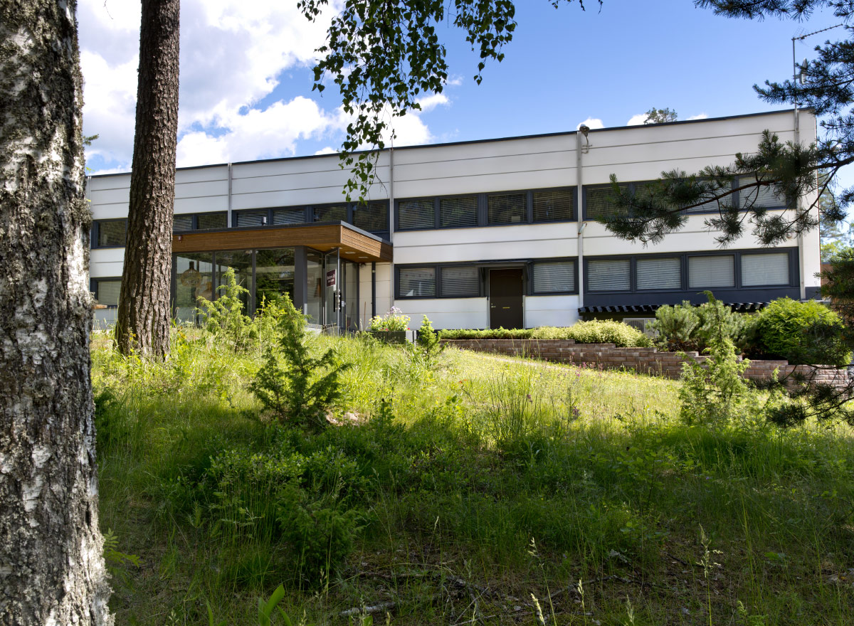 L'usine de Secto Designs vue de face avec quelques arbres, de l'herbe et de petits buissons au premier plan.
