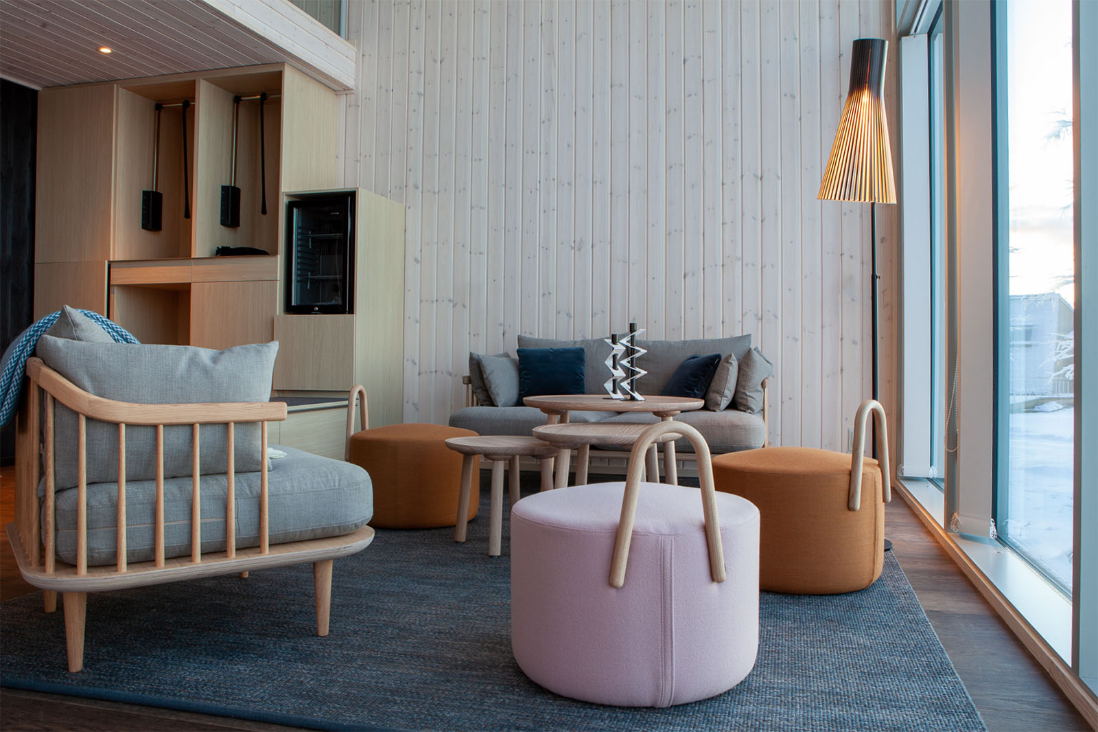 Un espace de vie aux meubles clairs et aux murs en bois, avec un lampadaire Secto placé près d’une grande fenêtre sur la droite.