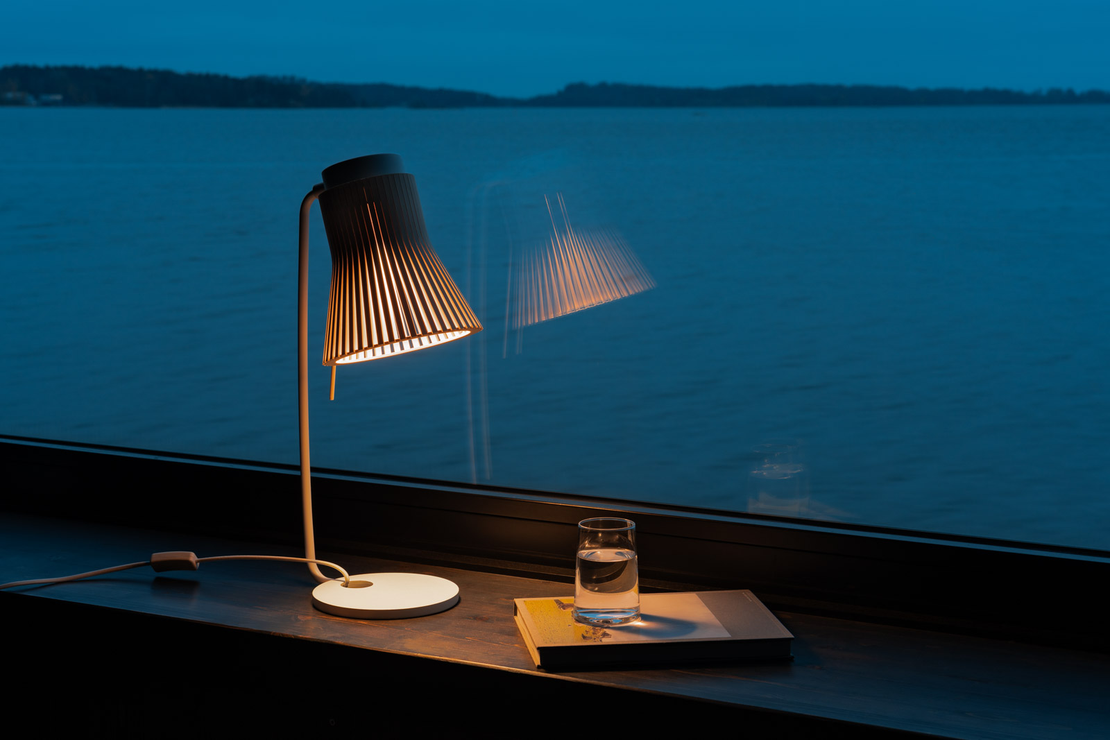 Lampe de table Petite sur un rebord de fenêtre en bois surplombant l'archipel d'Helsinki, montrant l'éclairage nordique en harmonie avec le paysage côtier naturel.
