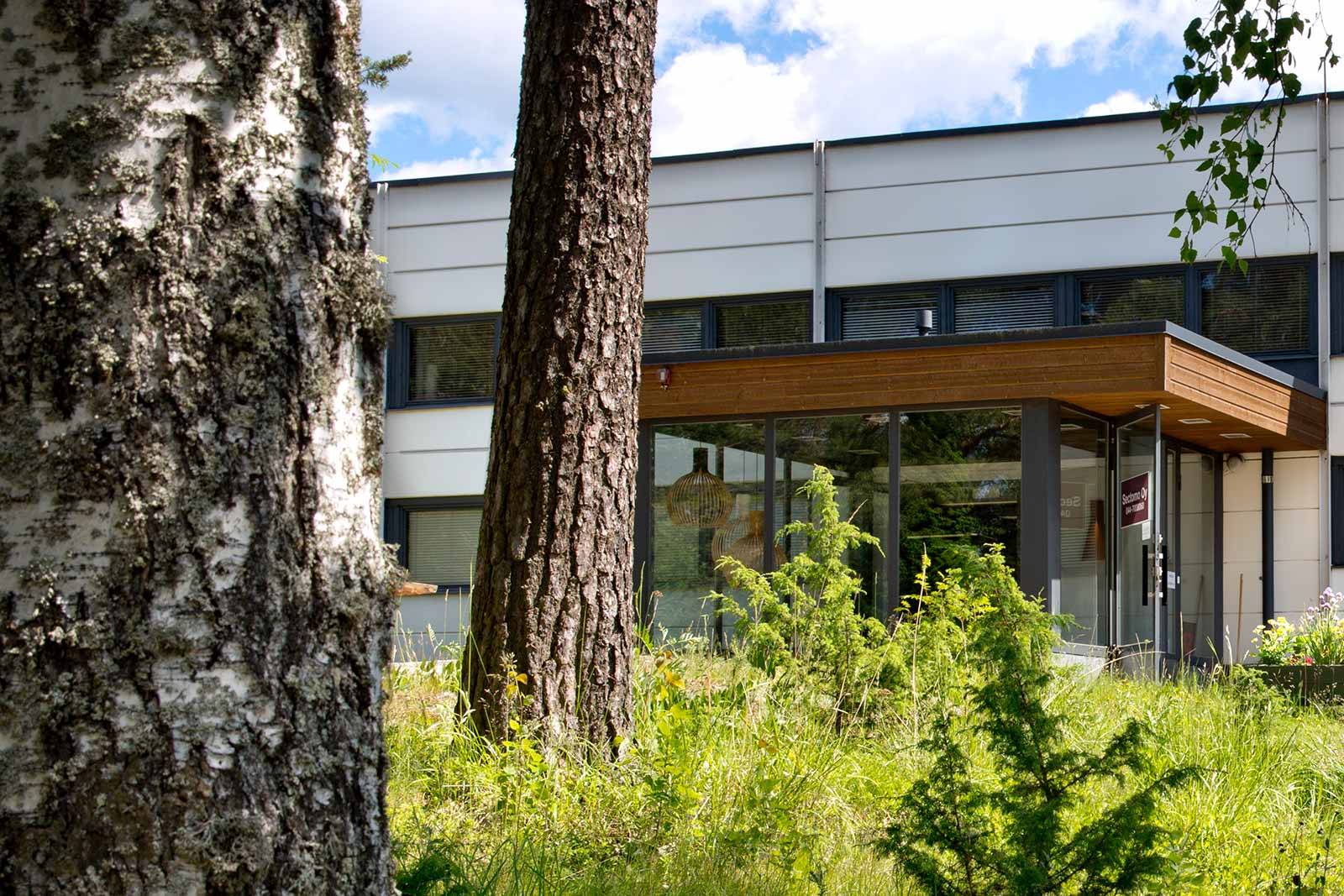 A front-view of the entrance to the Sectomo factory with some trees, grass and small bushes in the foreground.