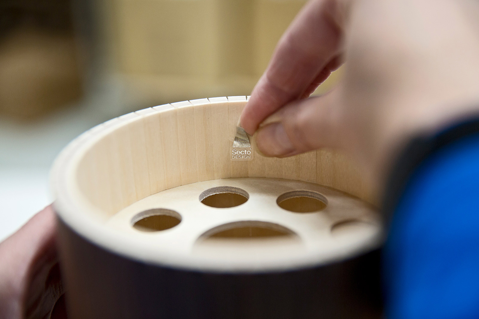 A hand is gluing the Secto Design hologram label inside the top of a lampshade.