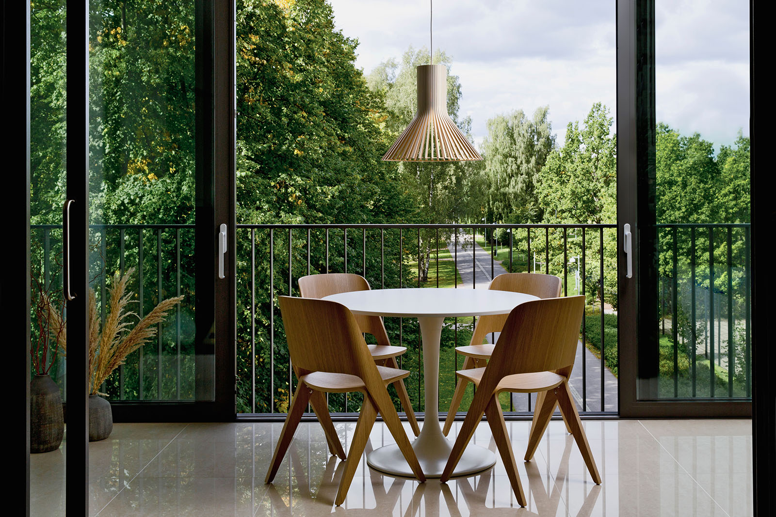 A round table and four chairs on a balcony. The Puncto pendant lamp is hanging above. There are trees in the background.