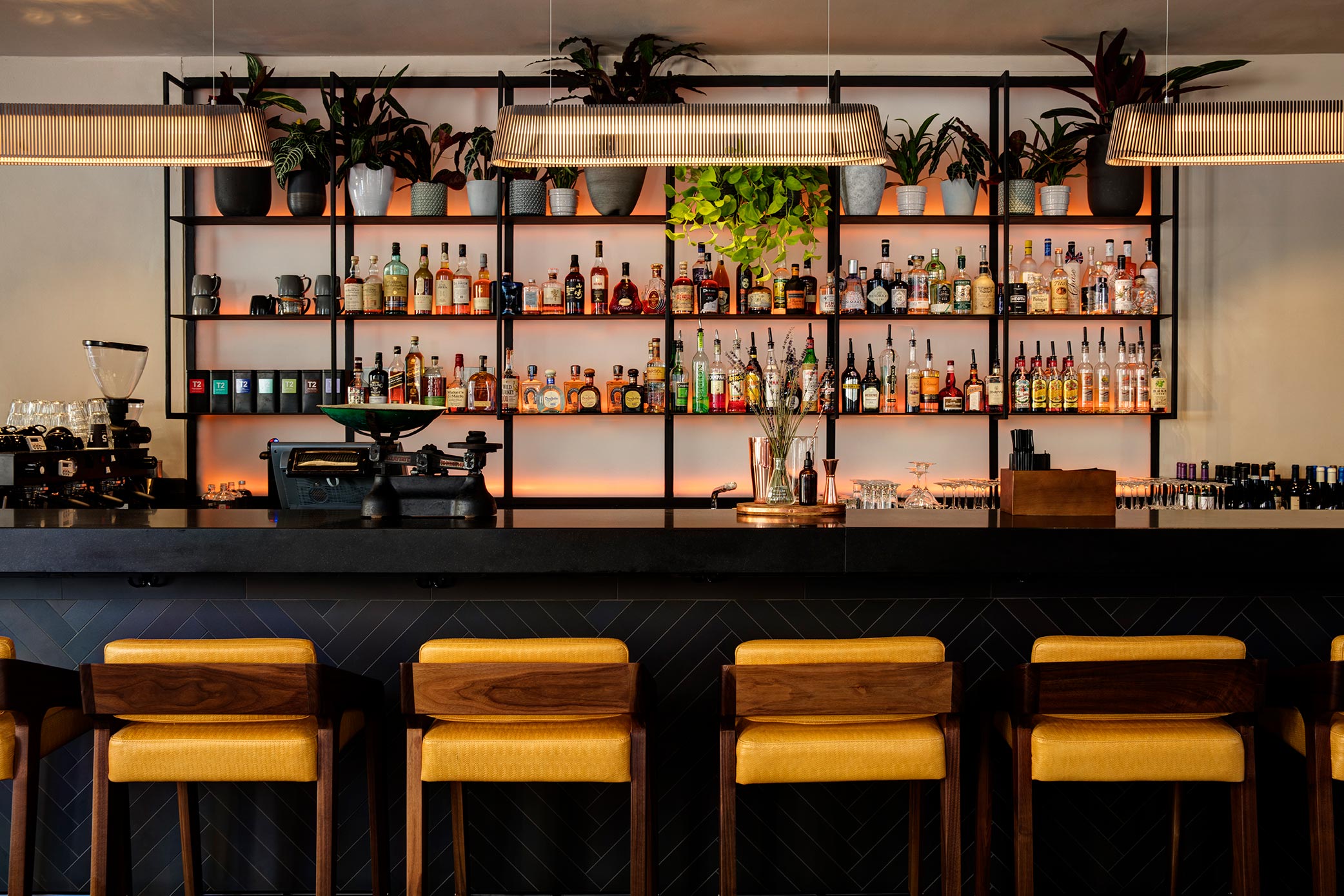 Owalo pendant lamps over a black bar and yellow chairs in front of it.
