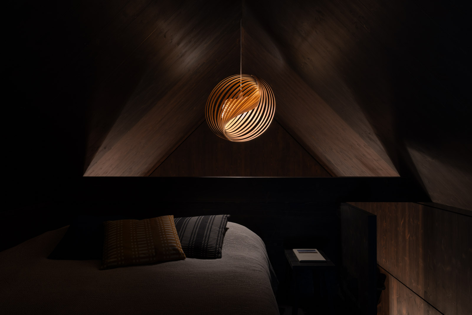 Adilo pendant lamp illuminating a dark, minimalist sleeping alcove in the Majamaja cabin, creating a warm and cosy Nordic interior atmosphere.
