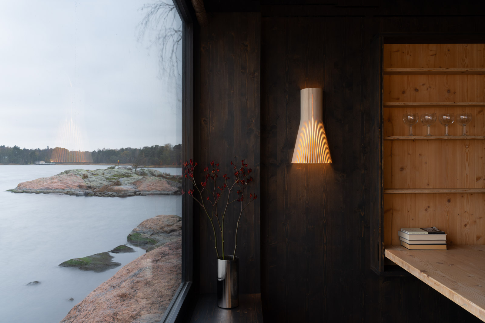 Secto Small wall lamp on a wooden wall overlooking the Helsinki archipelago, showing Nordic lighting in harmony with the natural coastal landscape.