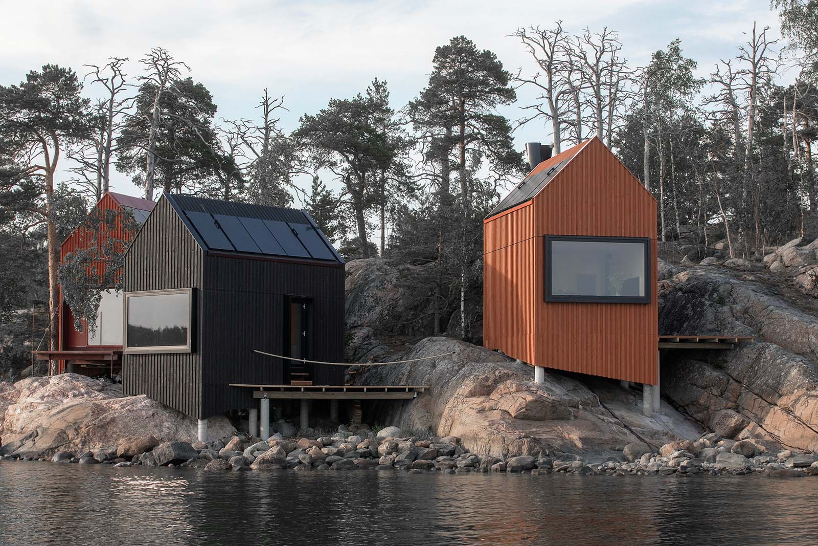 Majamaja wooden cabins seen from the sea, set on coastal rocks and blending naturally into the Nordic archipelago environment.