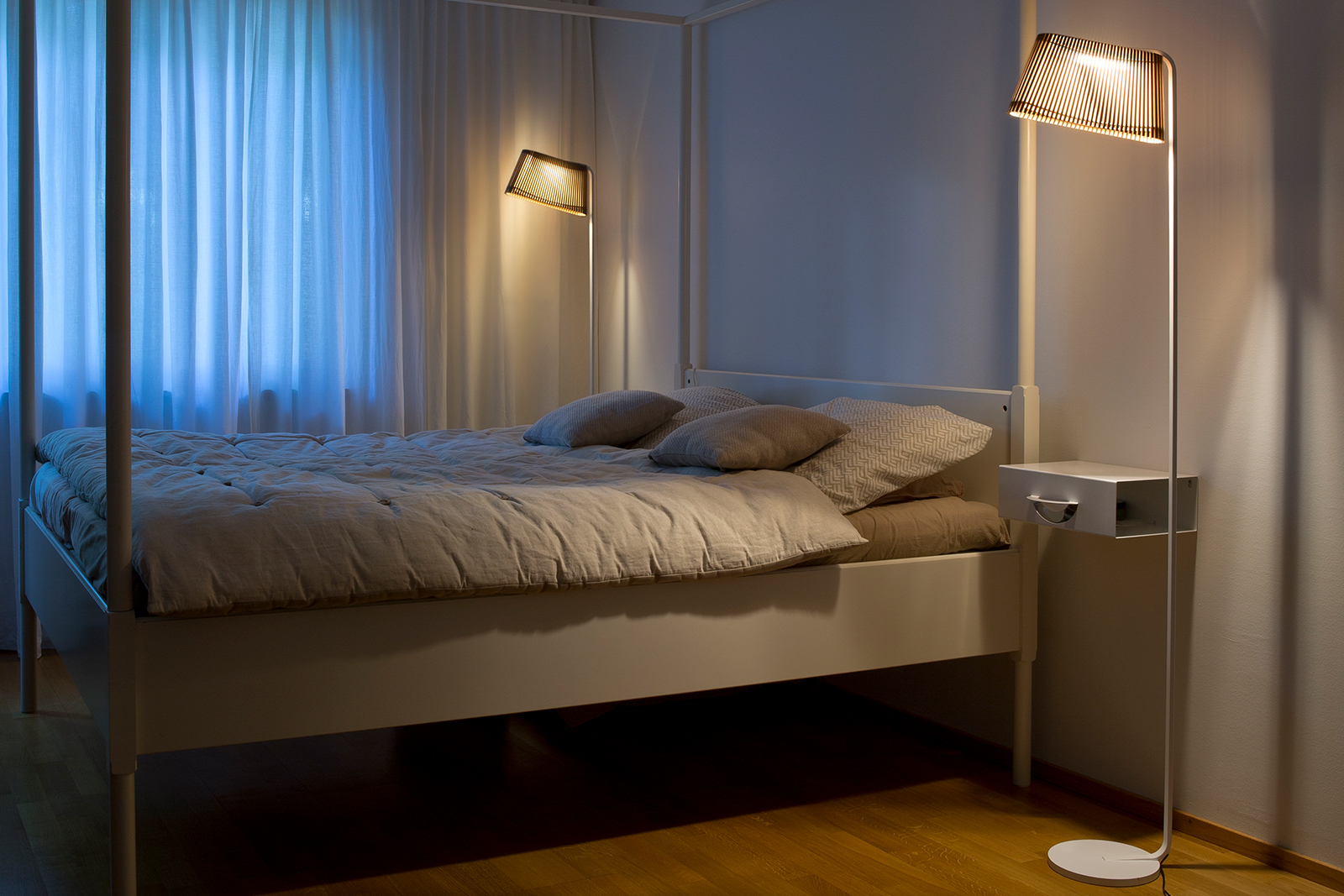 Floor lamps placed on the both sides of a canopy bed.