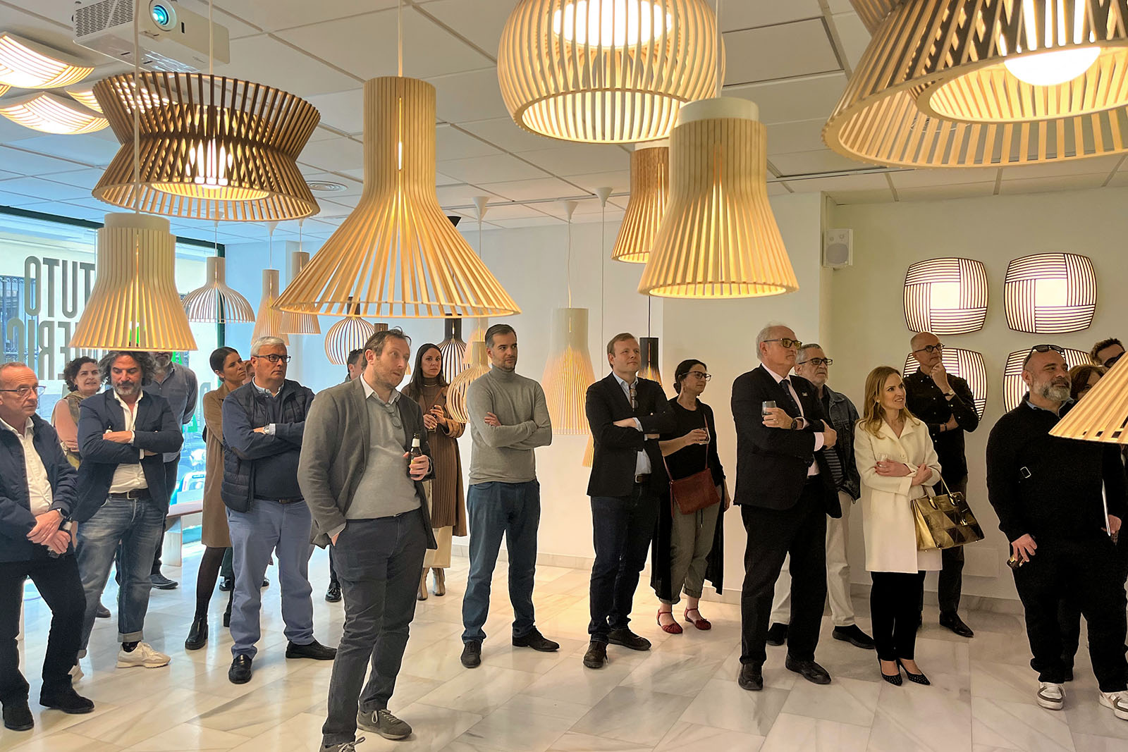 A group of people standing under wood lamps in a spacious room.