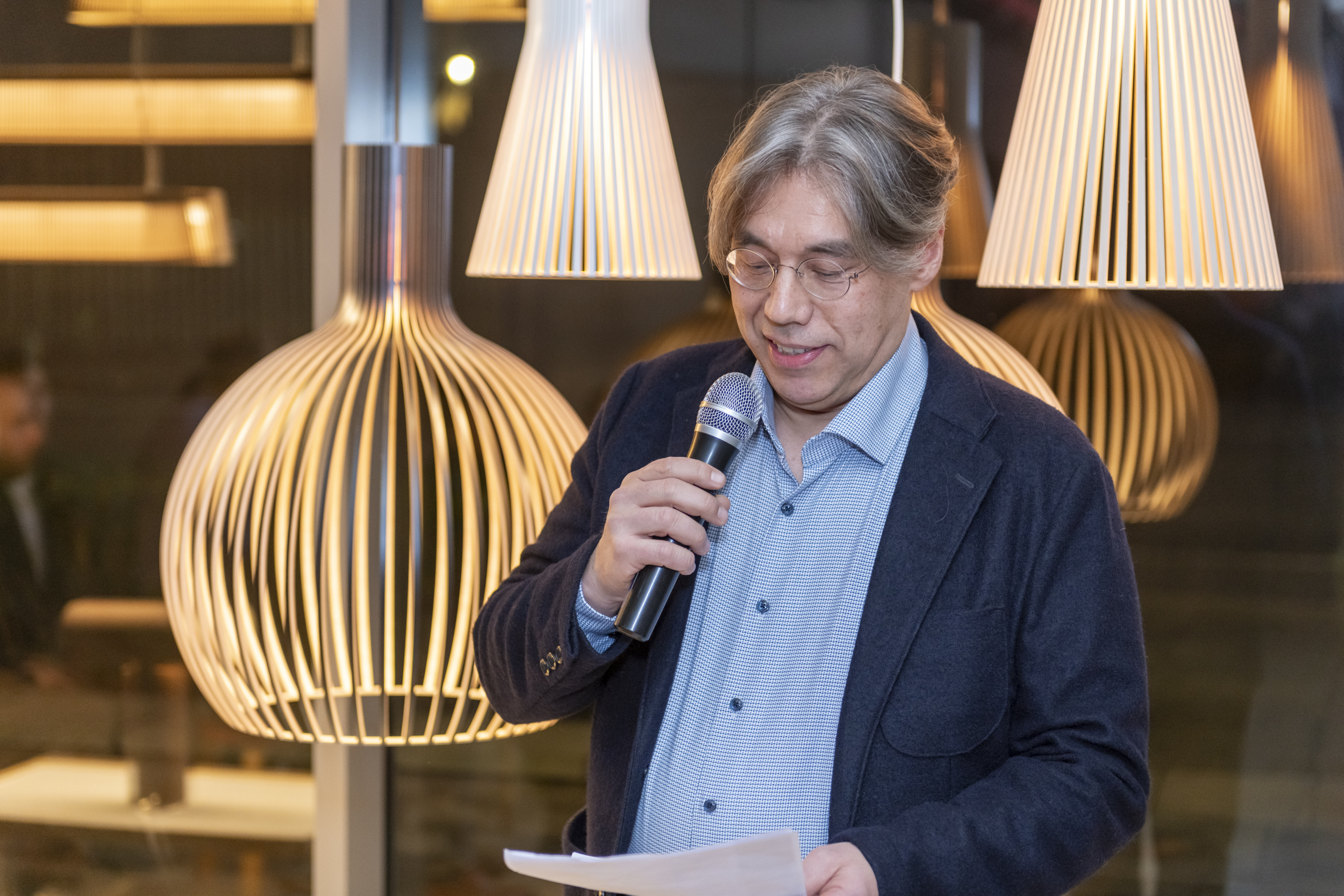 A man with a microphone in front of wooden lamps.