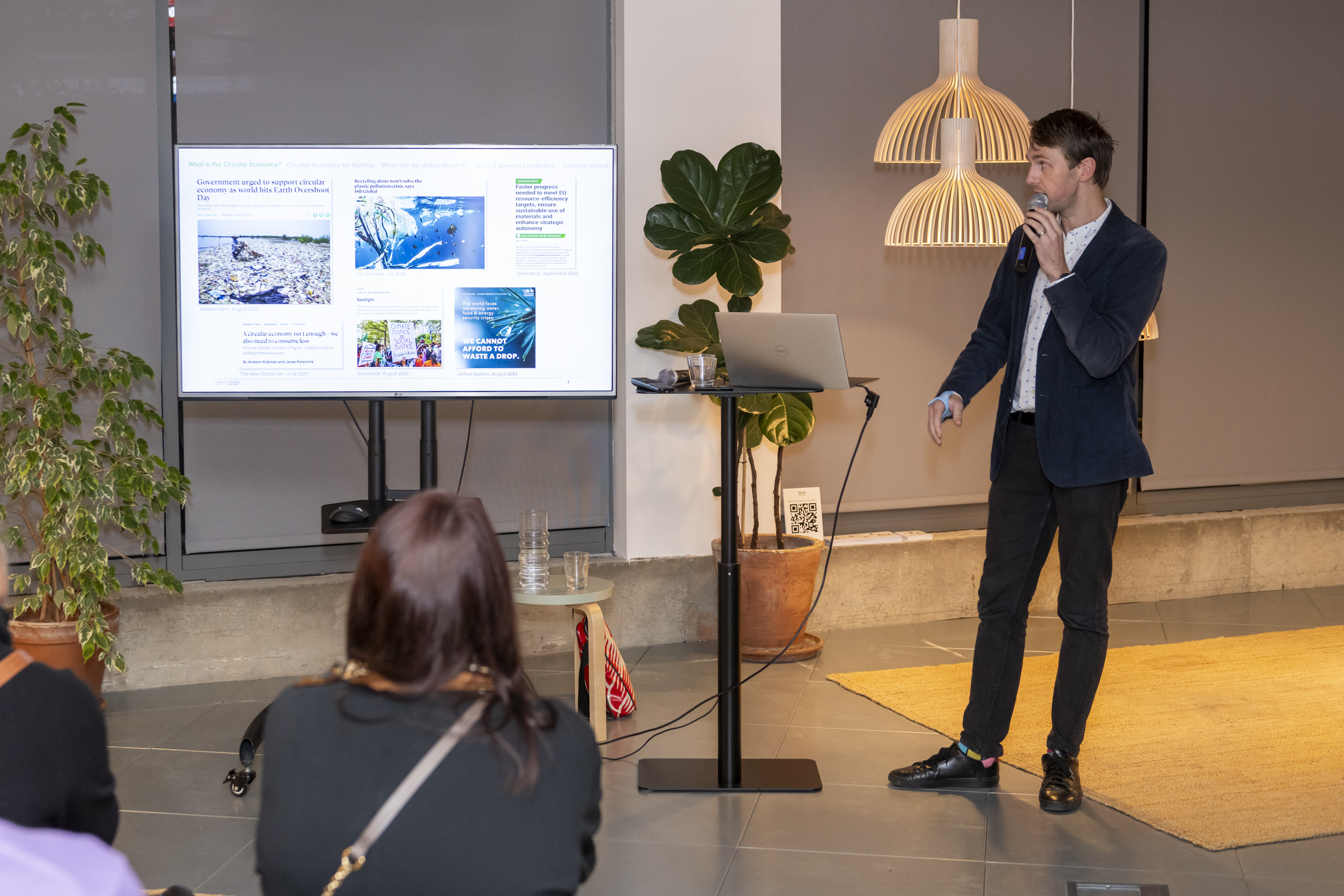 A man in front of the audience talking to a microphone while looking at a presentation on a screen. 