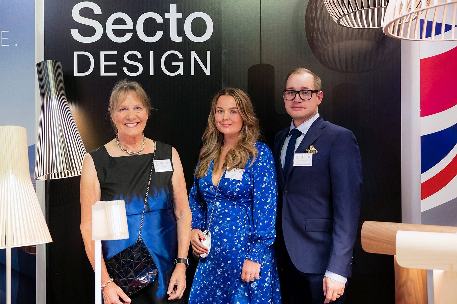 Wooden lamps and three smiling people in front of the company logo.